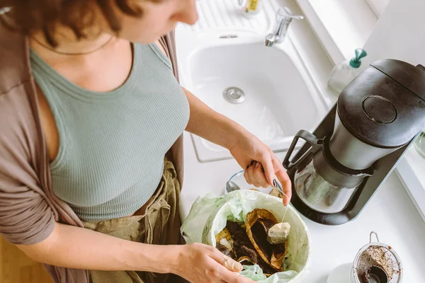 Yakından, farklı açılardan, kullanılmış çay poşetini mutfak mutfağındaki yiyecek kutusuna atan genç bir kadın. Evde atık ayıklama, geri dönüşüm, gübreleme