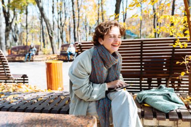 Sonbahar parkında bankta otururken videodaki neşeli genç kadın. Autumn Park 'taki mutlu genç kız laptopla video görüşmesi yapıyor. 