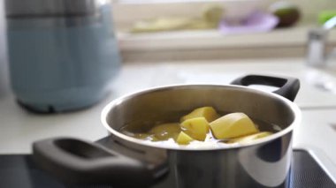 Ev mutfağında haşlanmış patates pişirmek. Kadın haşlanmış suya çiğ patates koyar, karıştırır, tuzlar, kontrol eder.