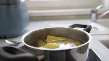Ev mutfağında haşlanmış patates pişirmek. Kadın haşlanmış suya çiğ patates koyar, karıştırır, tuzlar, kontrol eder.