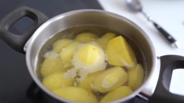 Ev mutfağında haşlanmış patates pişirmek. Kadın haşlanmış suya çiğ patates koyar, karıştırır, tuzlar, kontrol eder.
