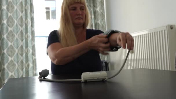 中年妇女 高血压 在家里用血压计检查血压 坐在桌旁 — 图库视频影像
