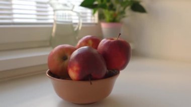 Kadın olgun, yıkanmış büyük kırmızı elmaları seramik kaseye koyar, ev mutfağında, yemek pişirmeye hazırlanır.