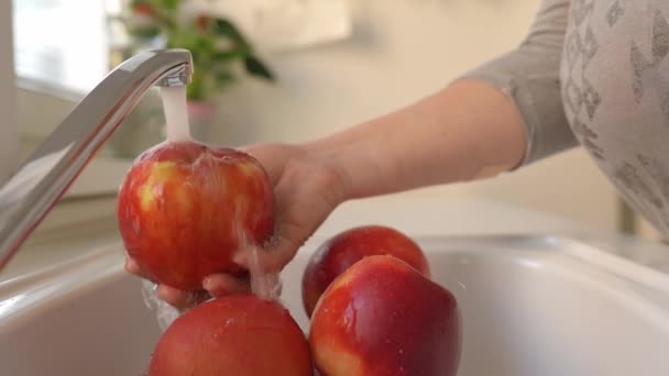 女性の手は ランニングウォーターの下でキッチンシンクで大きな赤いリンゴを洗います — ストック動画