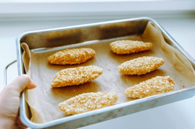 Fırın tepsisinde çiğ, donmuş tavuk parçaları. Ev yapımı külçeler için yarı bitmiş ürünler. Kadın eli, donmuş tavuk parçalarını hamurun üzerine serer.