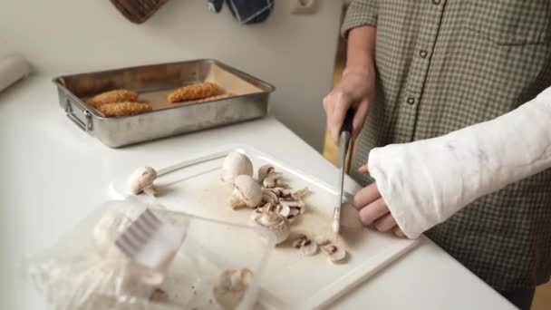 手挽手 在家里做午饭 年轻女子 手臂上有石膏 用菜刀在木板上切香菇 — 图库视频影像
