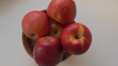 Kadın olgun, yıkanmış büyük kırmızı elmaları seramik kaseye koyar, ev mutfağında, yemek pişirmeye hazırlanır.
