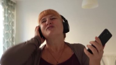 Orta yaşlı bir kadın evde, kulaklıkla müzik dinleyerek şarkı söylüyor.