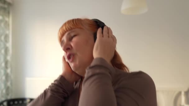 Orta Yaşlı Bir Kadın Evde Kulaklıkla Müzik Dinleyerek Şarkı Söylüyor — Stok video