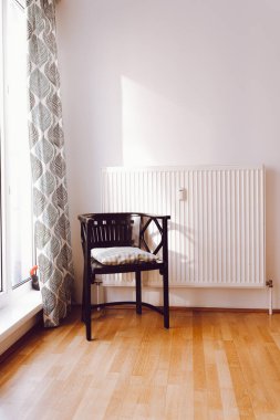 Parça halinde boş oturma odası, Fransız meşesi parke döşemeli, yastıklı rahat kahverengi koltuk perdeleri, beyaz duvarları ve radyatörü olan geniş parlak pencereli. Beyaz duvardaki ışık