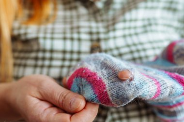 Kadın, eski yün bir çorapta yıpranmış, yırtılmış bir delik gösteriyor.