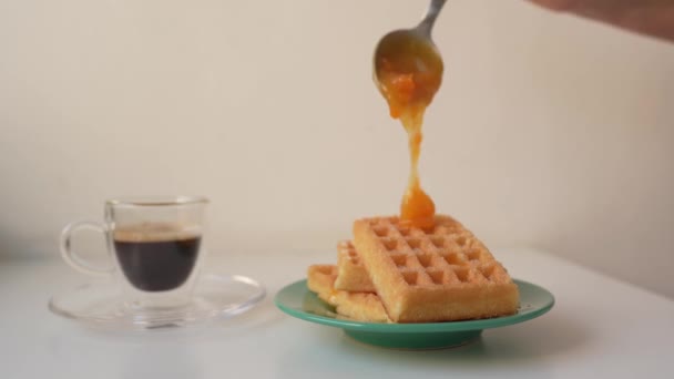 女人的手把杏仁或橙子果酱倒在比利时松饼上 一杯新鲜的香浓咖啡就站在它旁边 早上的甜早餐 — 图库视频影像