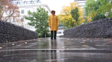 Sarı parlak yağmurluklu mutlu genç kızın portresi, çok güzel bir sonbahar yağmur parkında, su birikintilerinde zıplıyor, yağmurda dans ediyor.