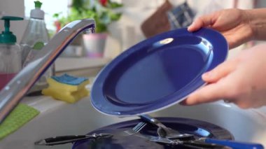 Modern mutfakta suyun altında mavi bir tabağı durulayan bir kadın.