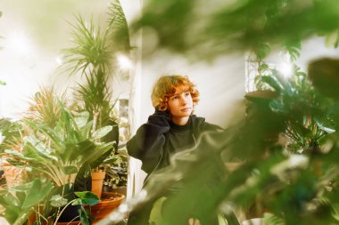 Çekici bir portre, kızıl saçlı ve serada kıvırcık saçlı pozitif bir genç kız.