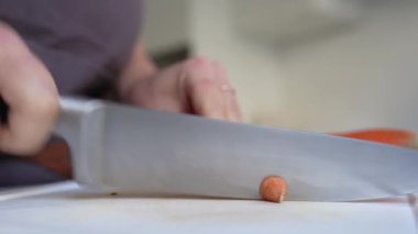 Kahverengi önlüklü tanınmayan bir kadın mutfak mutfağında büyük bir bıçakla havuç kesiyor..
