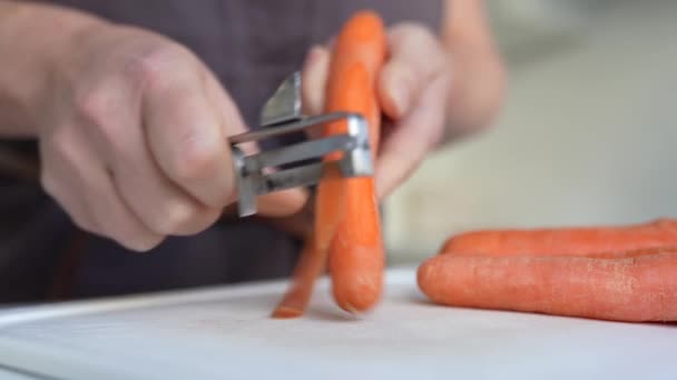 Неузнаваемая Женщина Коричневом Фартуке Чистит Морковь Ножом Кухне — стоковое видео
