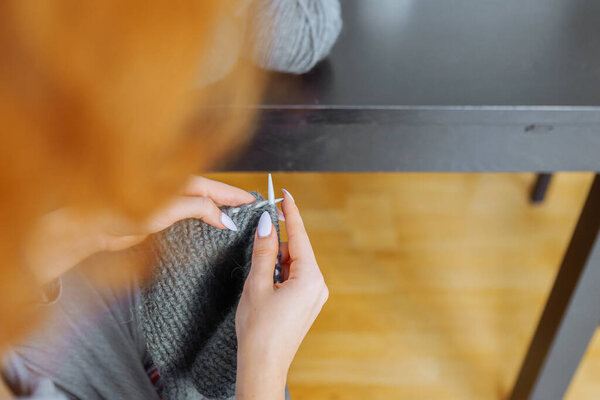 young woman knits wool product. hands an unrecognizable young woman with manicure knitting product from gray woolen thread