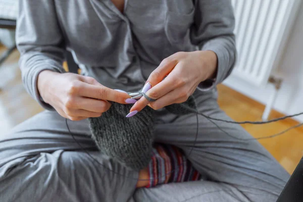 young woman knits wool product. hands an unrecognizable young woman with manicure knitting product from gray woolen thread
