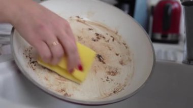 Kırmızı manikürlü eller kirli, kızarmış tava ve mutfak lavabosunda yağlı kahverengi lekeler. Bulaşık deterjanıyla tavayı yıkamak için bez kullanan kadın.
