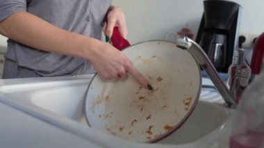 Ellerini lavaboda, mutfakta kirli yağlı tavayı yıkayan genç bir kadın.