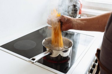 Erkekler spagettiyi sıcak suya bandırır. Ev mutfağındaki seramik hob 'un üzerinde durur.