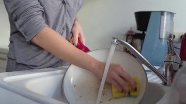 Ellerini lavaboda, mutfakta kirli yağlı tavayı yıkayan genç bir kadın.
