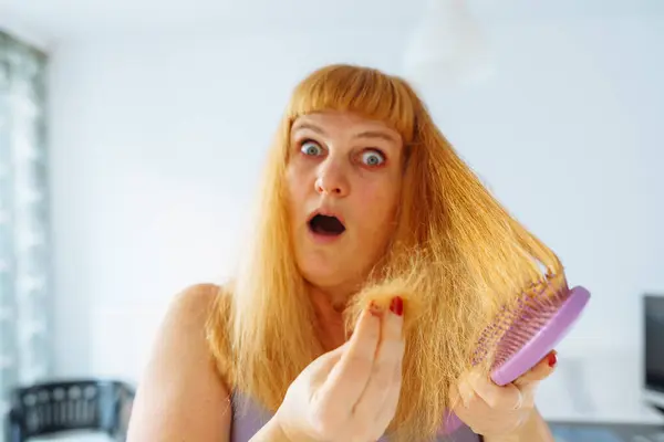 Portrait middle-aged woman with long red hair, with tuft fallen hairs on hairbrush, suffering from baldness, lack vitamins, aging, excessive hair coloring