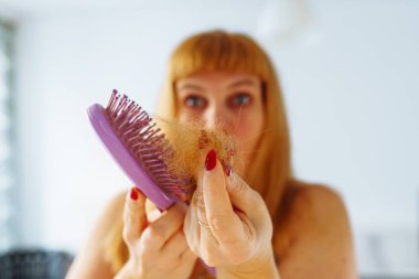 Uzun kızıl saçlı orta yaşlı bir kadın portresi, saç fırçasında tüy dökülmüş saçlar, kellik, vitamin eksikliği, yaşlanma, aşırı saç boyası