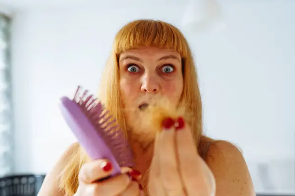 Portrait middle-aged woman with long red hair, with tuft fallen hairs on hairbrush, suffering from baldness, lack vitamins, aging, excessive hair coloring