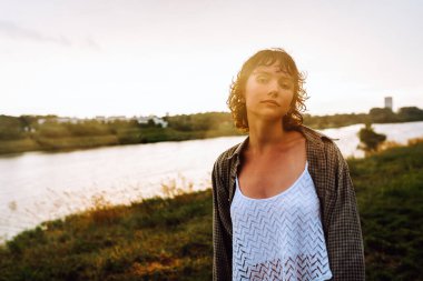 Su birikintilerinde çıplak ayakla dans eden Happy portresi, genç kız, ıslak saçlı, bol yaz kıyafetleri içinde, gün batımında, yağmurdan sonra, nehir kenarında. Doğadan zevk alma kavramı, gün batımı, özgürlük,