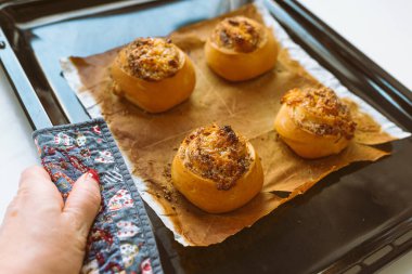 Tarçınlı çörekler yapmak, dört tarçınlı çörek pişirme kağıdı, çıtır çıtır kabuklu, kadınlar fırın eldiveni ve çöreklerle sıcak pişirme çarşafını tutarlar.