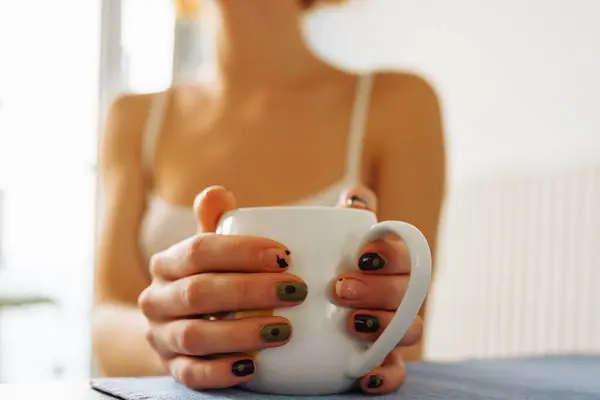 woman holds cup in hands, enjoying dishes and warmth it brings. hands young woman with peeled manicure
