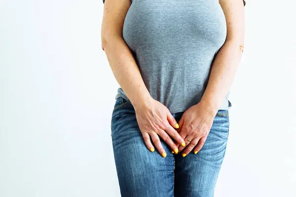 Gynecologic problems, urinary incontinence, female health. Woman holds hands between her legs. Unrecognizable middle-aged woman, wearing T-shirt and wet jeans, on white background