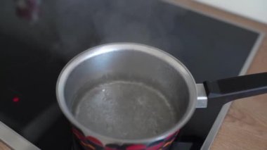 Bir indüksiyon yüzeyinde metal tavada buharla kaynayan su.