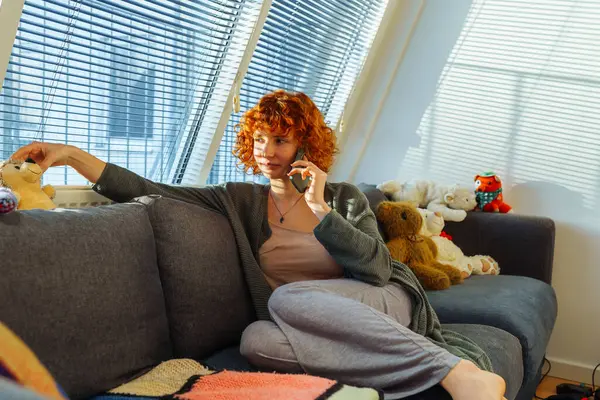 집에서 편안한 소파에 앉아있는 전화를 사용하여 초상화 블라인드와 아이들의 장난감 — 스톡 사진