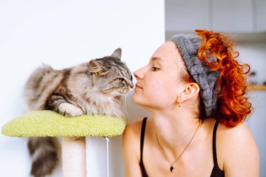 Kedi ağacında oturan gri tüylü kedi ve kızıl saçlı çekici genç kız, kedi sahibi. Birlikte zaman geçirmek, oynamak.