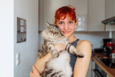 Portre kızıl saçlı genç kız gri tüylü kedi, pozitif ruh halinde, bulanık arka plan ev mutfağında