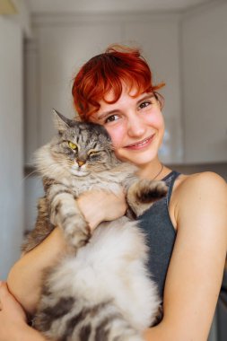 Portre kızıl saçlı genç kız gri tüylü kedi, pozitif ruh halinde, bulanık arka plan ev mutfağında