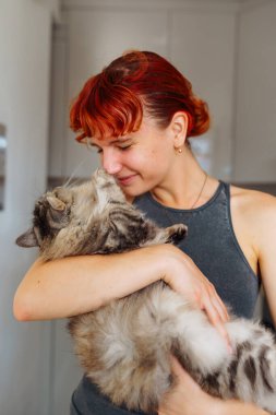 Portre kızıl saçlı genç kız gri tüylü kedi, pozitif ruh halinde, bulanık arka plan ev mutfağında