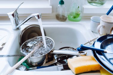 Kirli tabakları çatallarla, bardaklarla istifleyin, mutfak lavabosunun yanında durun, mutfakta beyaz cephelerle. Lavabonun yanındaki mutfak masasında yıkanmamış bulaşıklar.