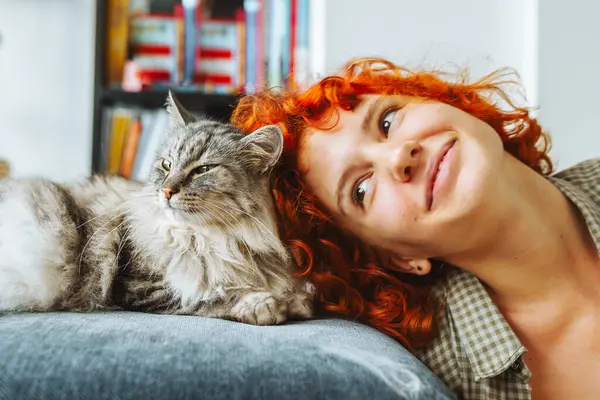Portre kızıl saçlı, çekici genç bir kadın pofuduk büyük kediyle sarılıyor. Şefkat gösterisi, mırıldayan büyük kedi. evcil hayvanla arkadaşlık