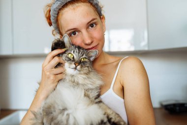 Portre kızıl saçlı genç kız gri tüylü kedi, pozitif ruh halinde, bulanık arka plan ev mutfağında