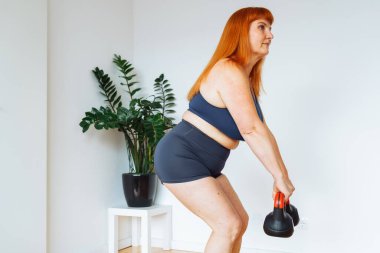 Evde çıngıraklı yılanlarla evde antrenman yapan son sınıf öğrencisi pozitif bir kadın, boş yer. Spor tişörtlü, şortlu, kıvrımlı, aktif bir hayat süren, kilo veren olgun bir kadın.,