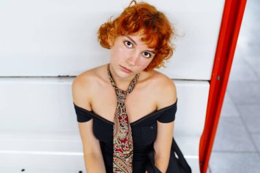 Gen z estetik kıyafeti havalı, hareketli ya da modaya uygun görünüm için. Tasarımcı markası. Kızıl saçlı, sıra dışı giysileri olan, kravatlı, serbest stil giysileri olan genç bir model, metroda. anime biçimi