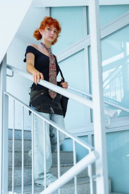 Merdivendeki kızıl saçlı çekici genç kadının portresi. Arkaplanda geniş bir vitrin var. Şık giyinmiş genç bir öğrenci, olağanüstü bir görünüş.