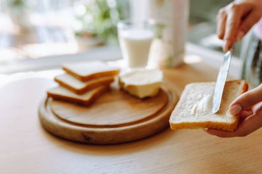 Sağlıklı kahvaltı sütlü ekmek ve tereyağı. Genç kadınların elleri kızarmış ekmeğe tereyağı sürüyor. Arka planda bir bardak taze süt var.
