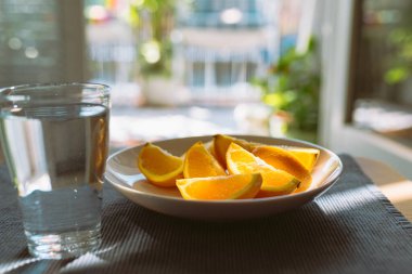 turuncu mono diyeti. Soyulmuş portakal dilimleri tabakta ve temiz su bardakları masada, güneş ışınlarında.