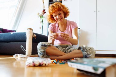 Genç kızıl saçlı kadın odanın zemininde oturuyor, talimatlara göre inşaat setini kuruyor, boş zamanlarını en sevdiği hobisine tutkuyla harcıyor.