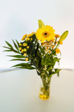  Gerbera çiçeği, kasımpatı, zambak. Sonbahar çiçekleri beyaz masada cam bir fincanda.